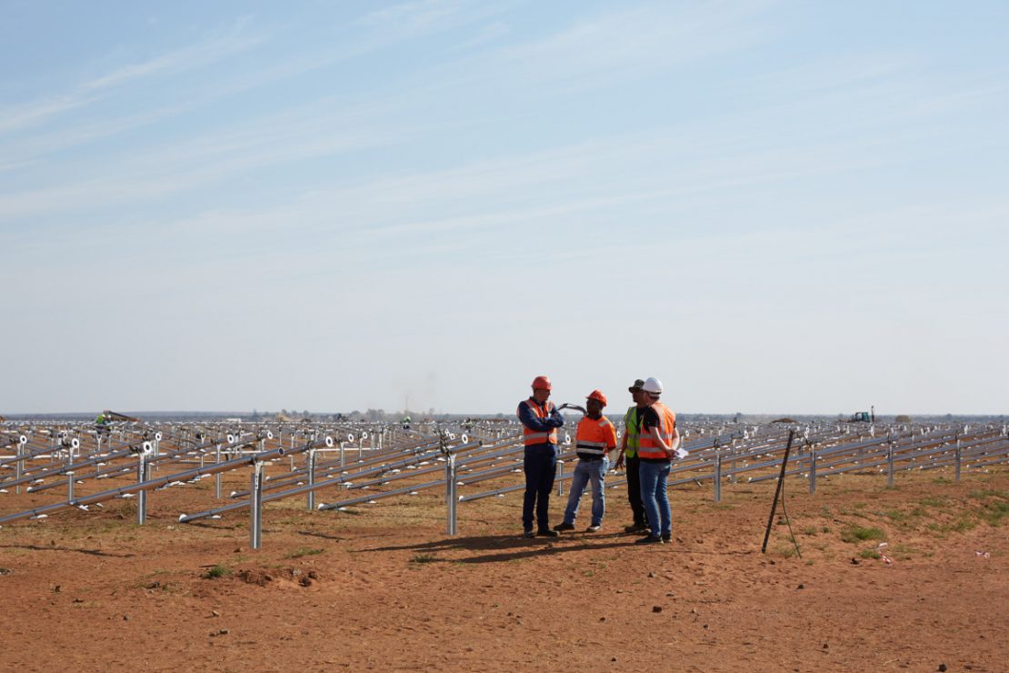 Vier Bauarbeiter unterhalten sich vor einer Solarparkanlage im Bau