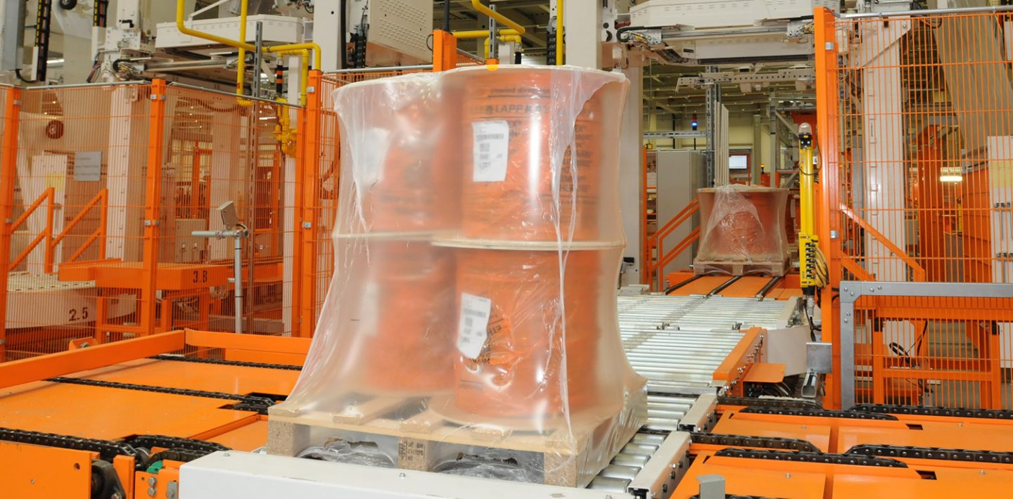 The picture shows a packaging line with a film-shrunk cable drum.