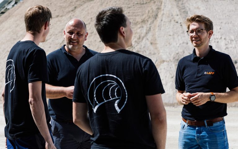In the picture you can see 4 people standing together: Patrick Olivan, LAPP Senior Business Development Manager (right), Alois Heimler, LAPP Business Development Manager Automotive (2nd from left) and two members of the TUM Boring Team.