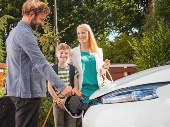 Auf dem Bild sieht man eine Familie vor einem Elektroauto, der Vater steckt das Ladekabel ins Auto.