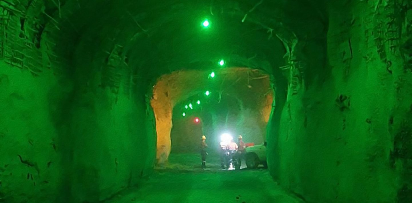 The picture shows a green-lit tunnel in an underground mine.