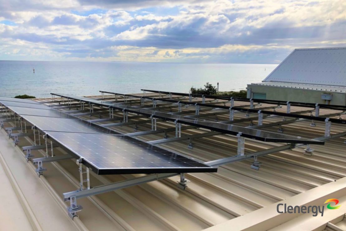 The picture shows a solar system on a roof with a view of the sea.