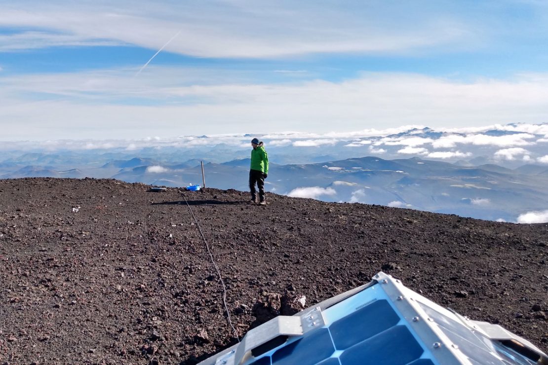 Das Bild zeigt Dr. David Craig am Gipfel des Vulkans, wo man auch eine Messhütte des isländischen Wetterdienstes sieht.