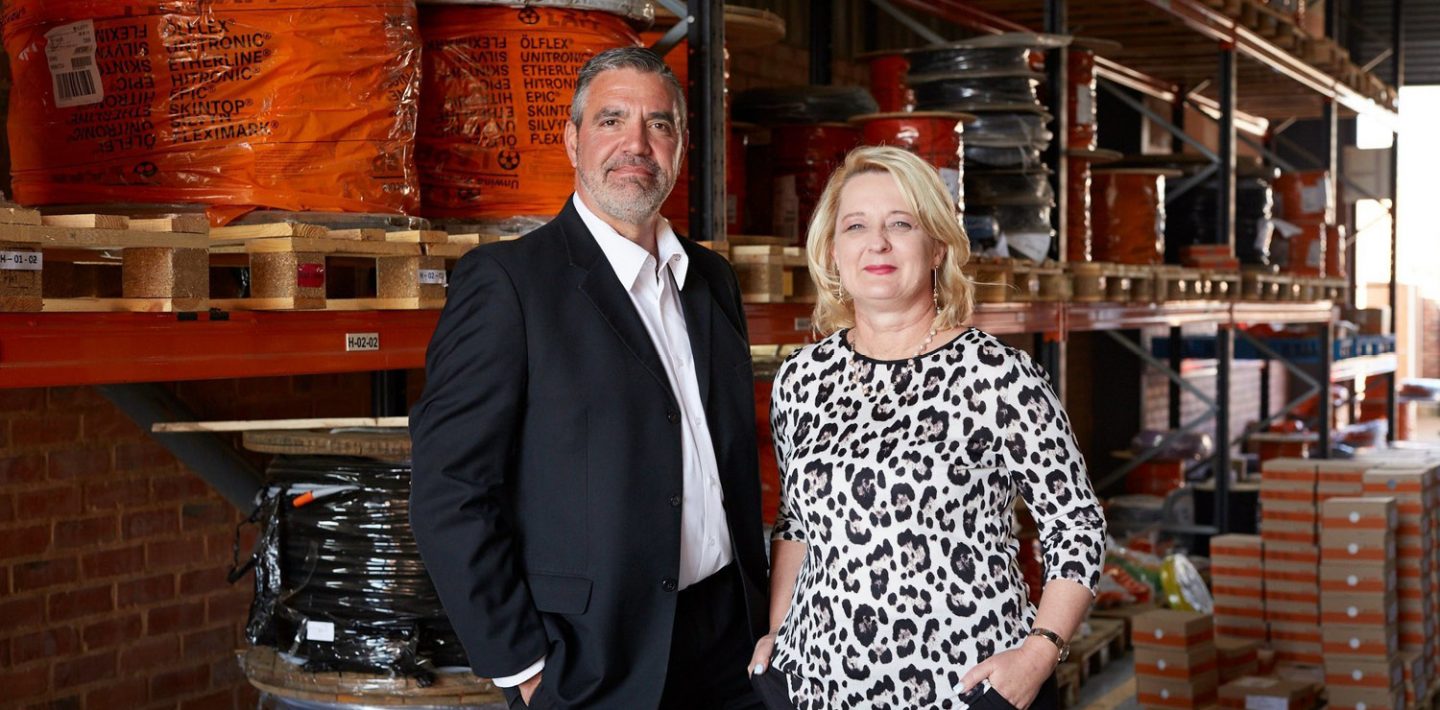 The picture shows the LAPP Southern Africa Management Team: Venessa Botha, Head of Finance & HR (right), Chad Andrews, Managing Director (left) in the warehouse in front of shelves with cables.