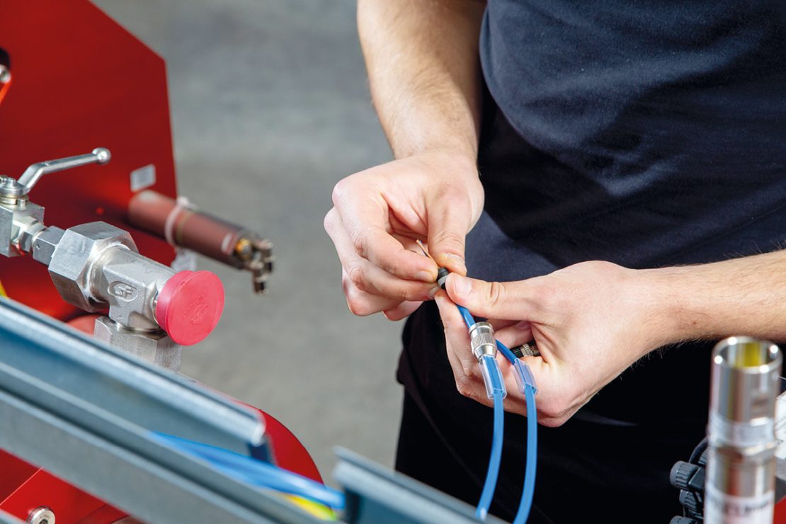 The picture shows a man with cables in his hands wiring hydrogen filling stations.