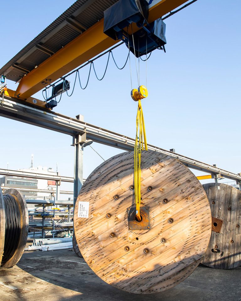 The picture shows a cable drum hanging from a heavy-duty crane.