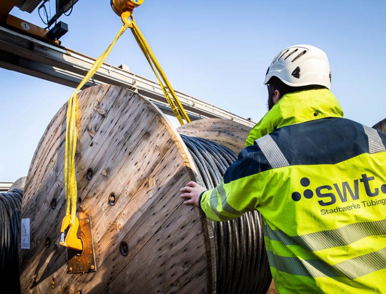 The picture shows an employee from Stadtwerke Tübingen moving a cable drum with a heavy-duty crane.