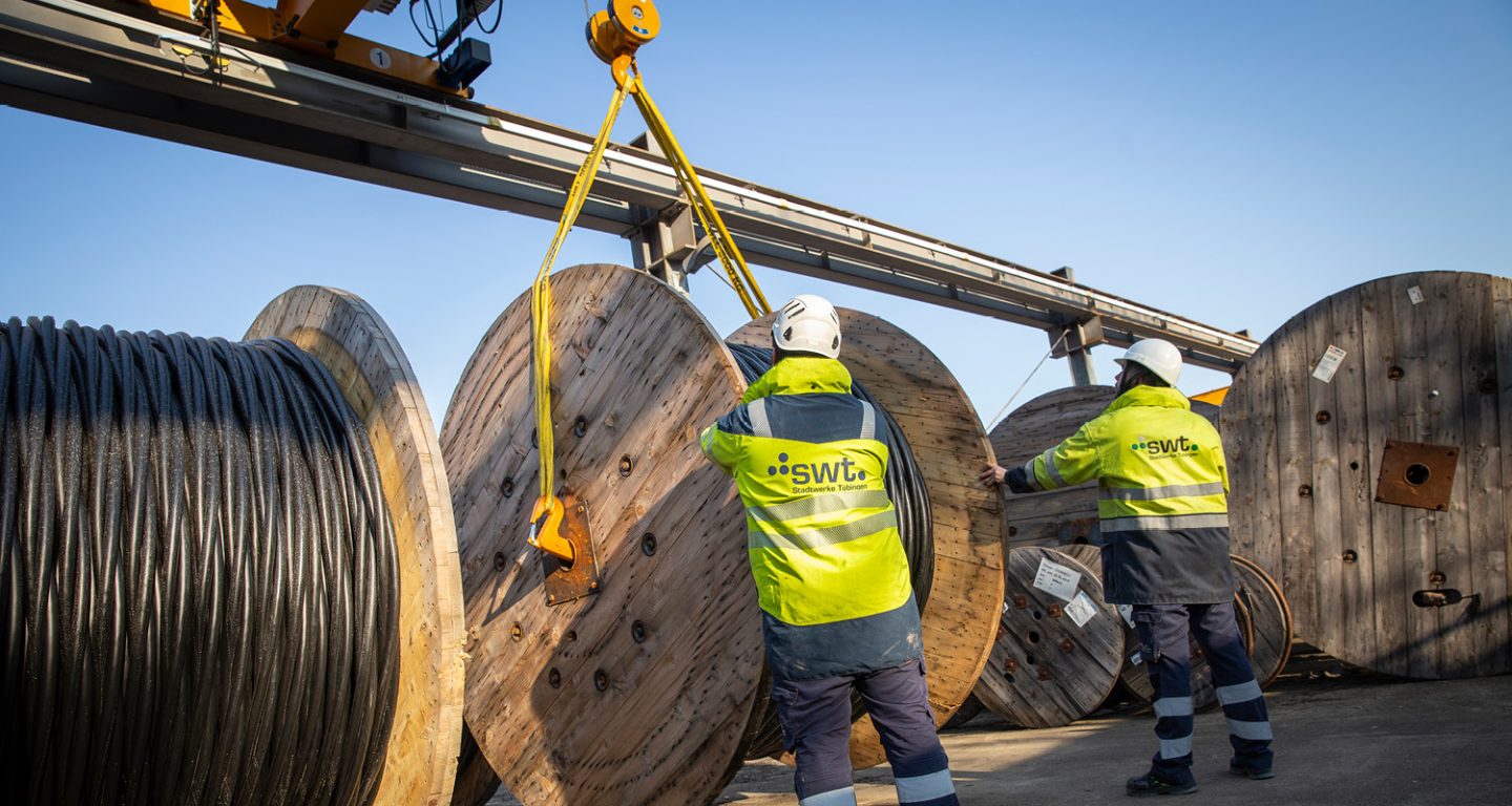 The picture shows two employees from Stadtwerke Tübingen moving a cable drum with a heavy-duty crane.