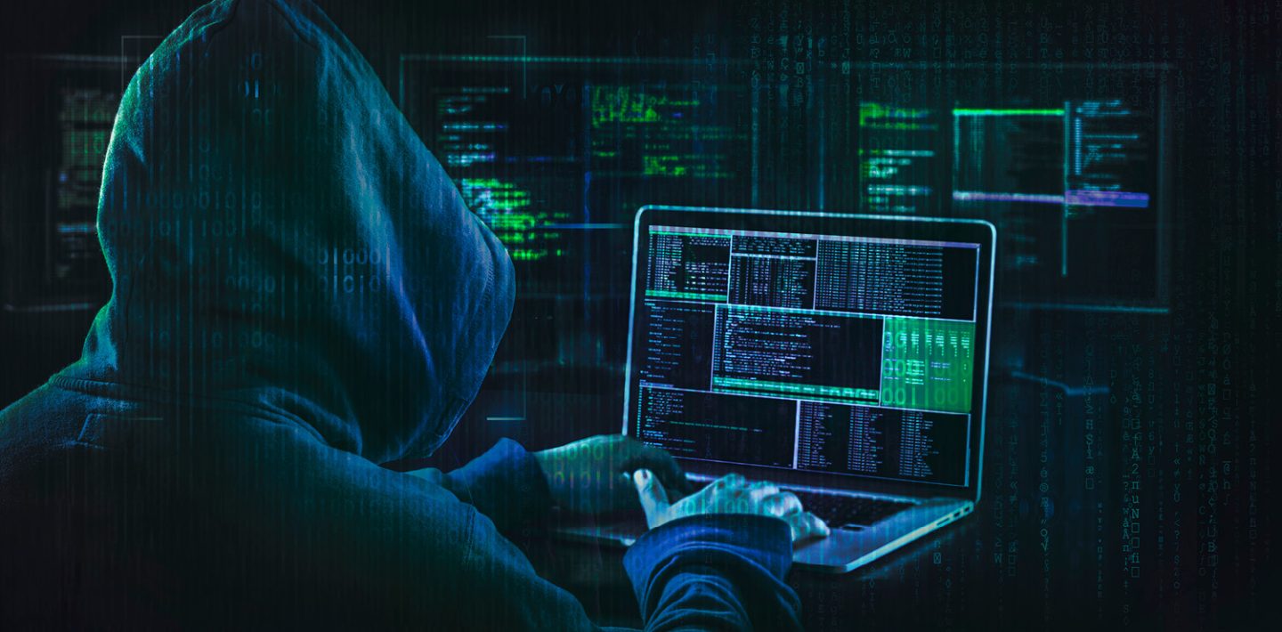 The picture shows a hacker with a hood in front of a computer.