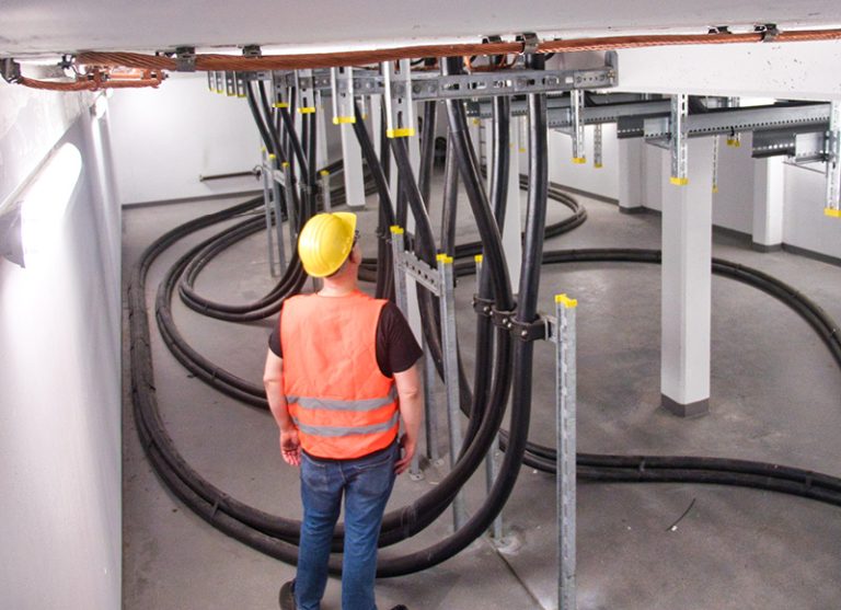 In the picture you can see a worker examining several thick pipes in the basement.