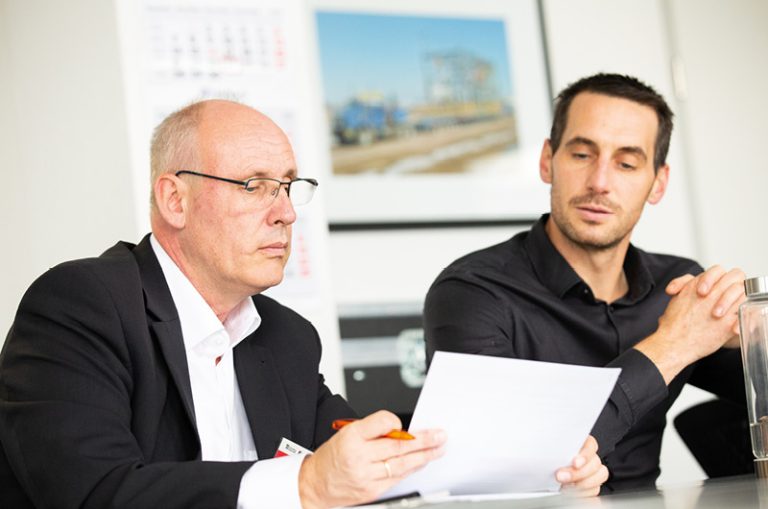 Das Bild zeigt Joachim Hentschel, Account Manager bei LAPP (links) und Tobias Maier, Teamleiter Steuerungstechnik beim TII-Tochterunternehmen TII KAMAG, in einer Besprechung am Tisch.