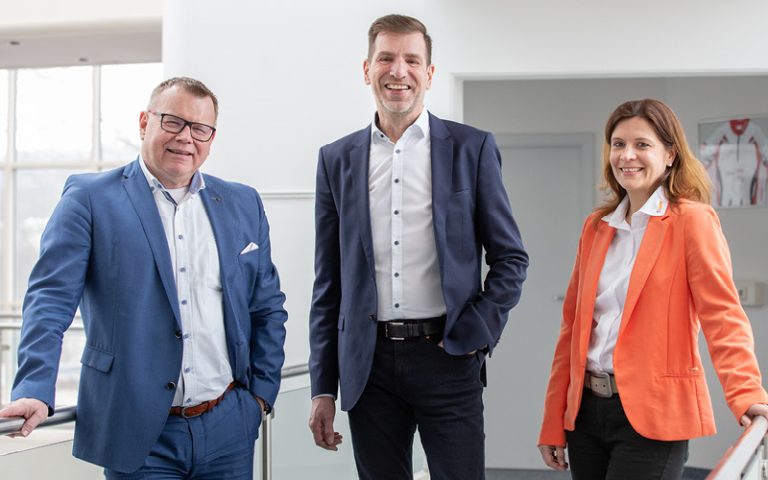 Das Bild zeigt Ingolf Oßfeld – Global Head of Purchase and Logistics bei der aichele GROUP GmbH + Co. KG, Thorsten Grünberg – Industry Manager Train bei der U.I. LAPP GmbH und Bianca Feistel – Account Managerin bei U.I. LAPP GmbH im Gang der Fertigung der era-contact GmbH am Standort Bretten-Gölshausen.